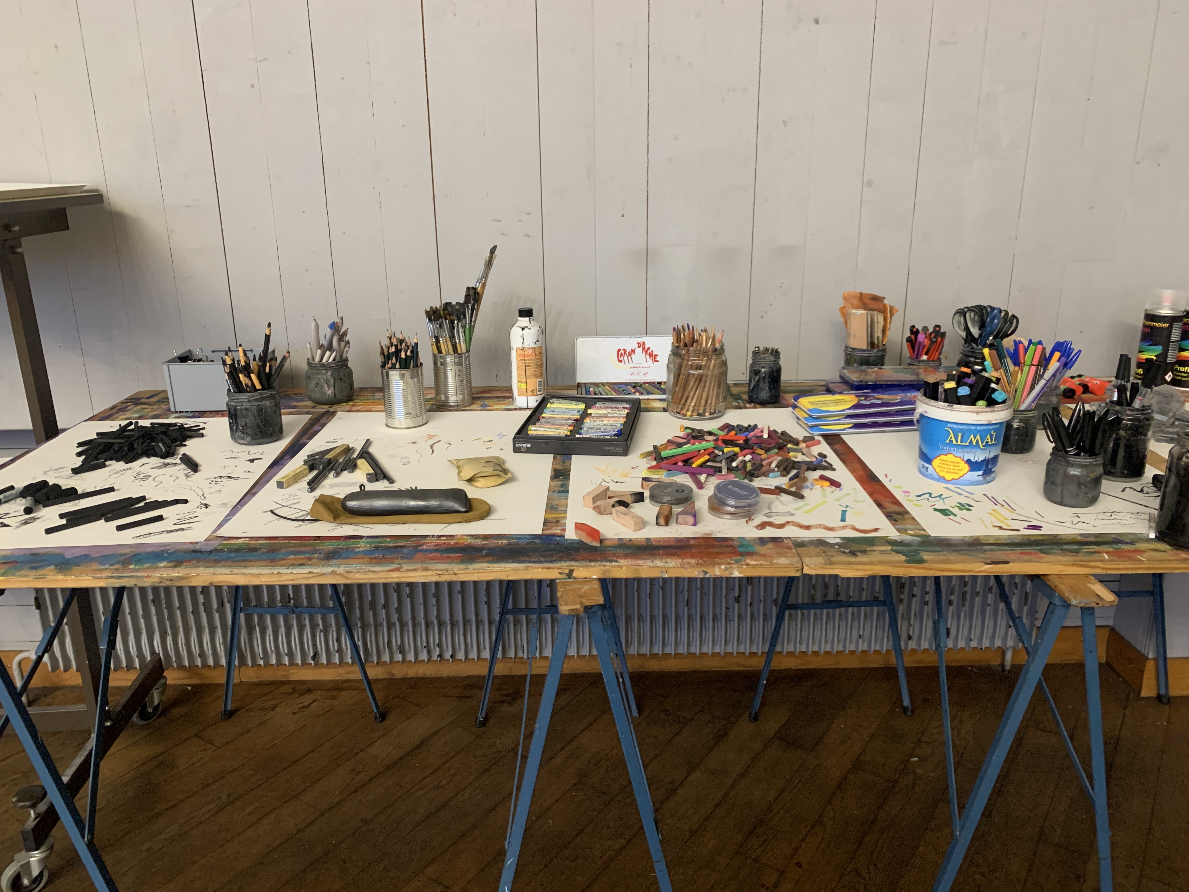 Cluttered workbench with various drawing supplies spread across a blue folding table