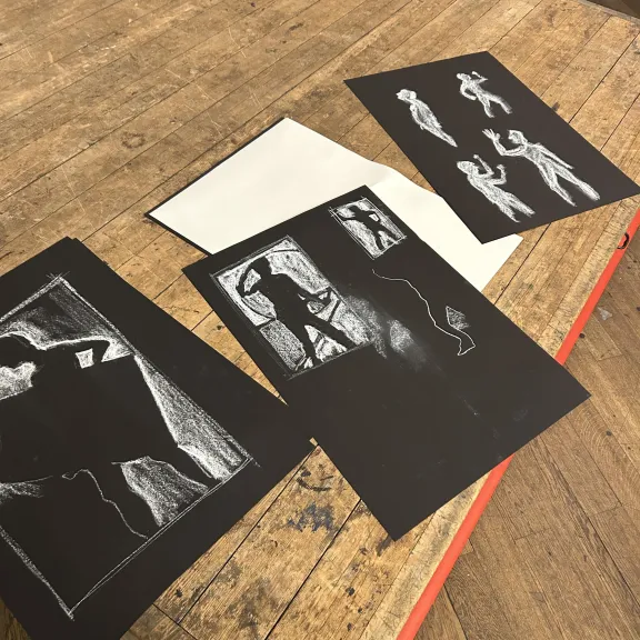 Three black and white performance illustrations laid out on a wooden table surface
